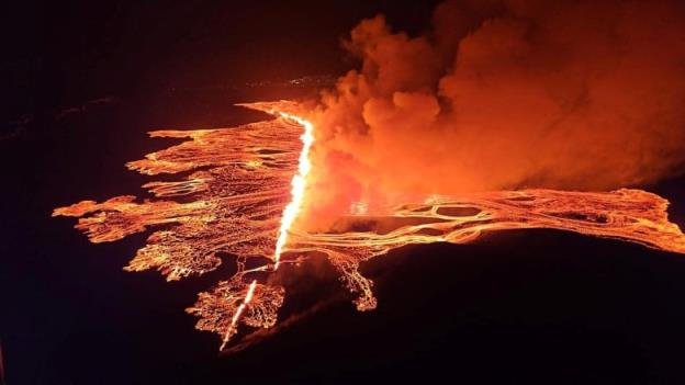 An aerial view shows lava flowing and smoke billowing during a volcanic eruption.
